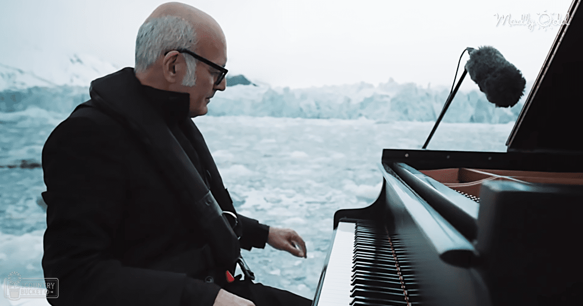A middle-aged adult male plays a grand piano in an icy mountainous landscape.