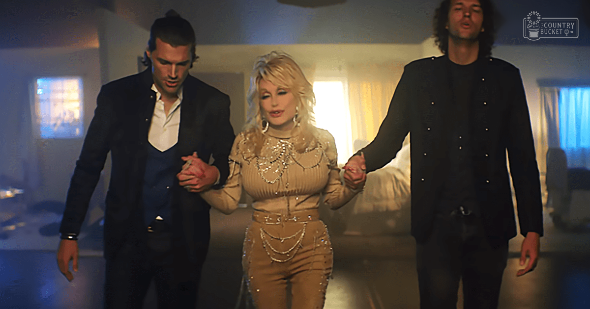 A middle-aged woman in a beige sequined top and pants set stands center, flanked by two men in suits; the indoor setting has soft lighting with furniture and curtains visible.