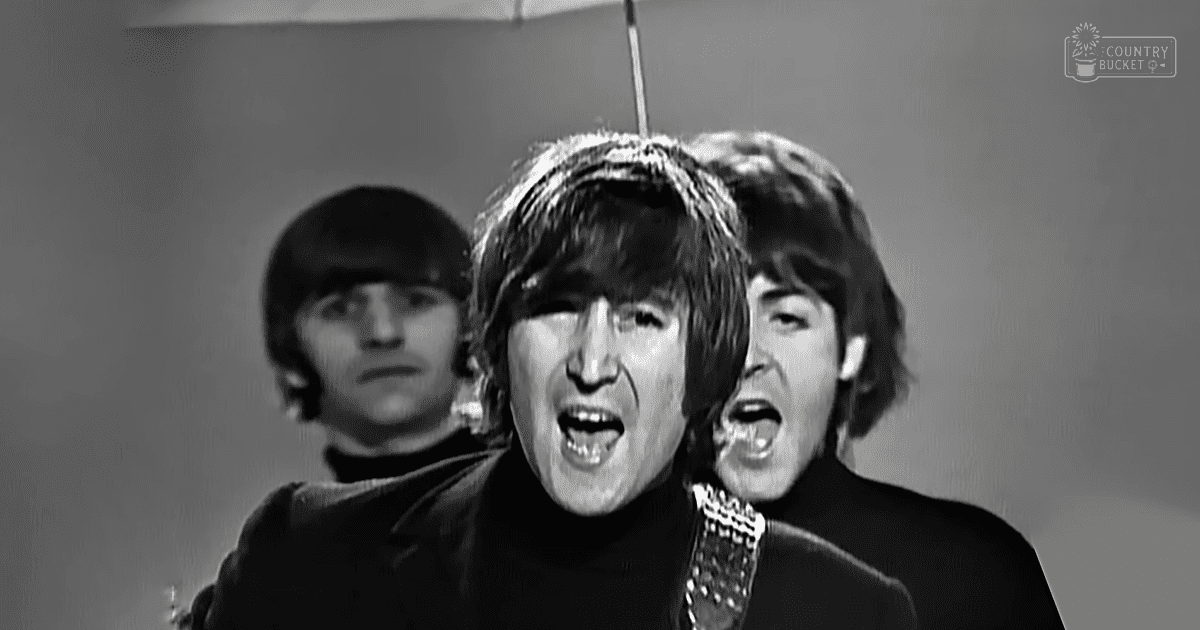 A young adult male wearing a textured black turtleneck sweater indoors with another similarly dressed individual in the background.