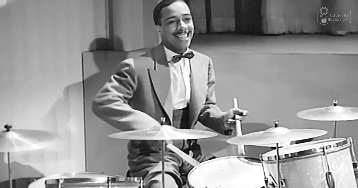 A man playing drums on a stage, dressed in a classic mid-20th century suit with a bow tie and white shirt.