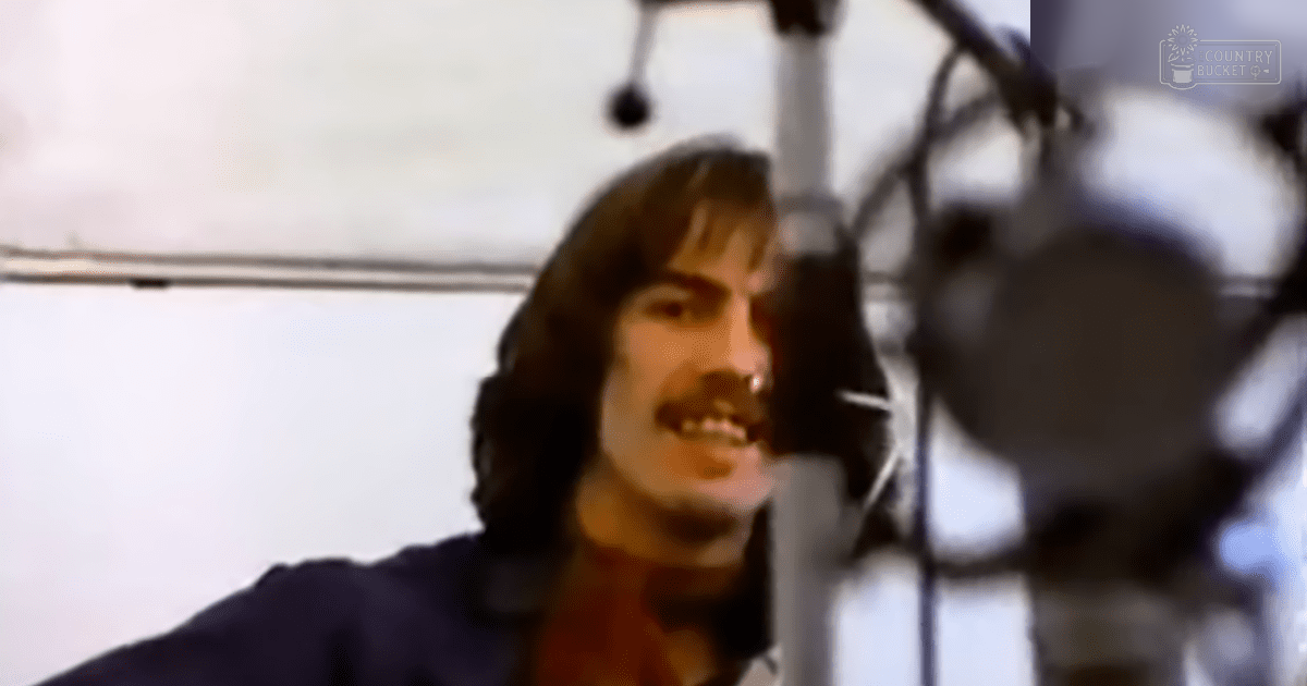A young adult male in a recording studio wearing a relaxed fit, collarless, short-sleeved dark-colored shirt with solid color and cotton blend fabric.