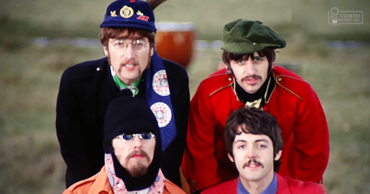 Four adult male musicians in an outdoor setting with blurred greenery behind them; they are wearing jackets of various colors including dark blue, red, and orange.