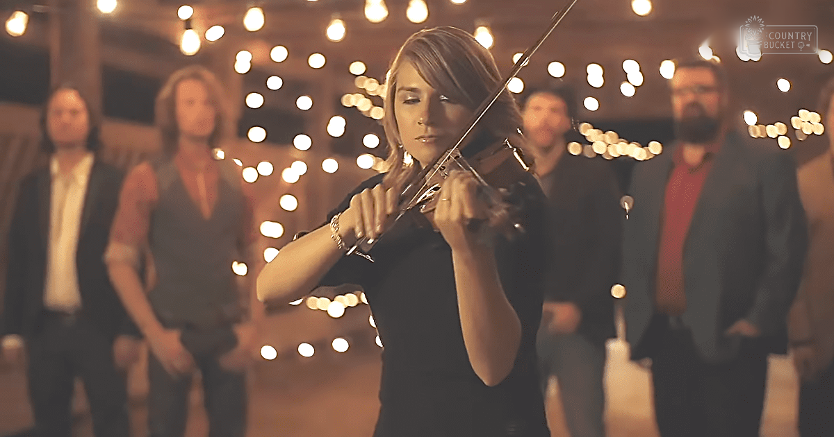 A young adult female playing a violin in an indoor setting with string lights.