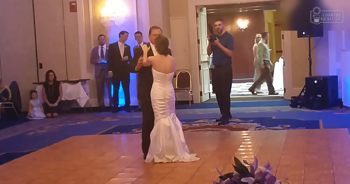 A bride and groom dancing at an indoor wedding reception with neutral walls and carpeted floors under artificial evening lighting.