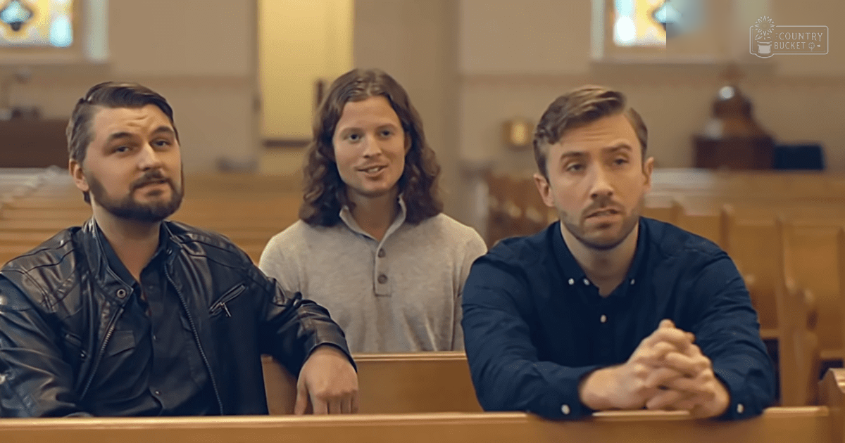 Three adults seated indoors, possibly in a church or chapel setting with wooden pews and stained glass windows; soft natural light illuminates the space.