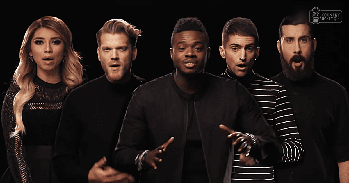 Group of performers wearing coordinated black outfits against a dark background, possibly at an event or studio setting.