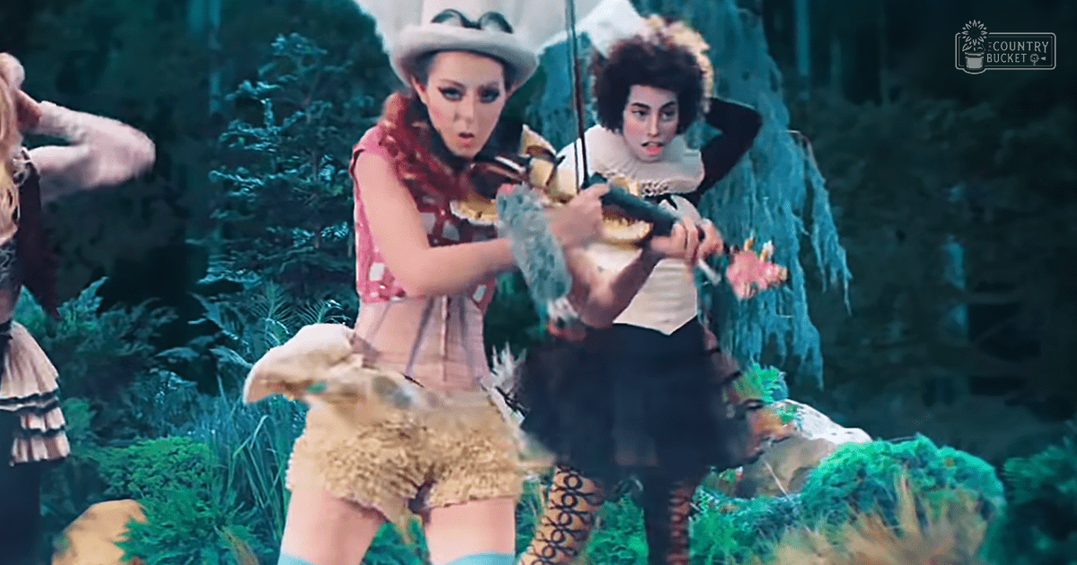 A scene from 'Alice in Wonderland' with a young adult female wearing a frilly pink dress, another young adult female in a white blouse and black skirt, and a white rabbit with brown patches in a fantastical forest setting.