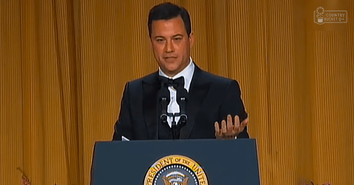Adult male in a formal setting with a podium with the Presidential Seal, indoors with vertical gold curtains.