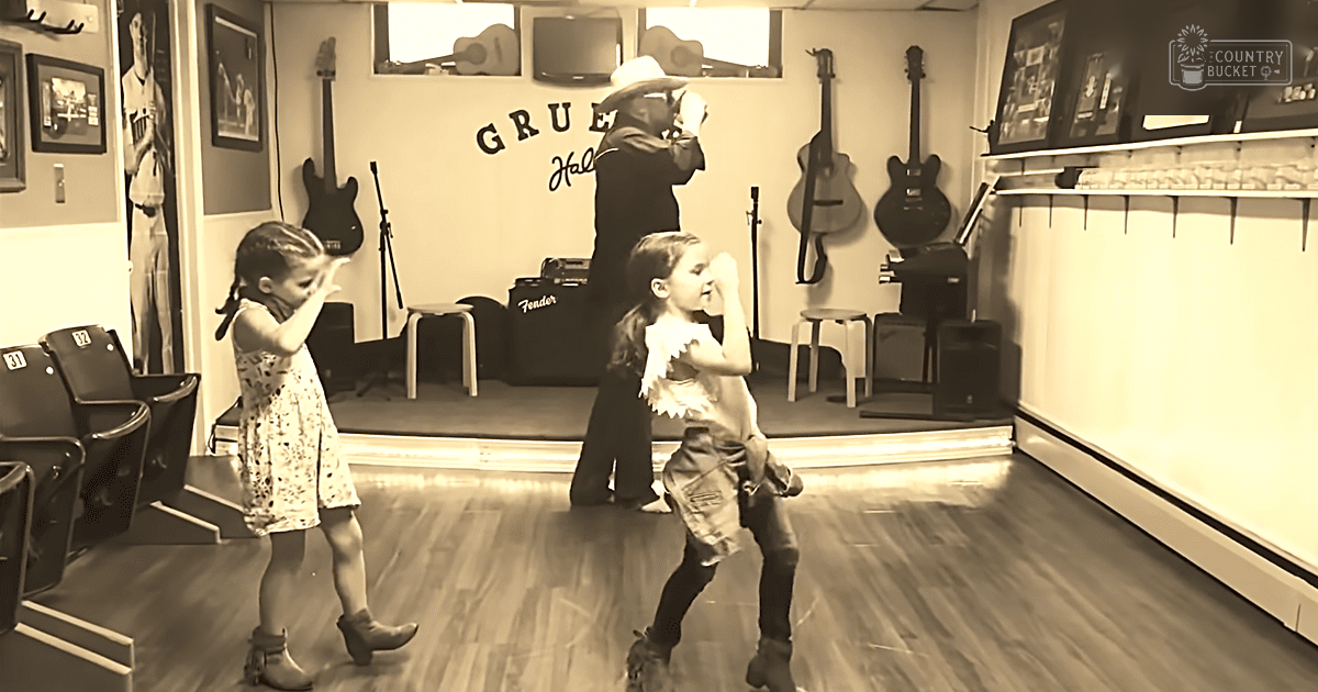 A family scene in a music studio or practice room with children wearing casual and cowboy-themed attire, surrounded by musical equipment and framed posters.