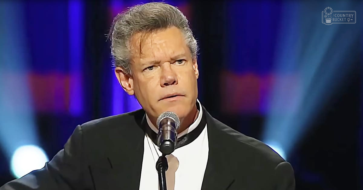 A middle-aged adult male wearing a tailored black suit jacket and white shirt on stage with 'Madly Odd' text visible in the top right corner.