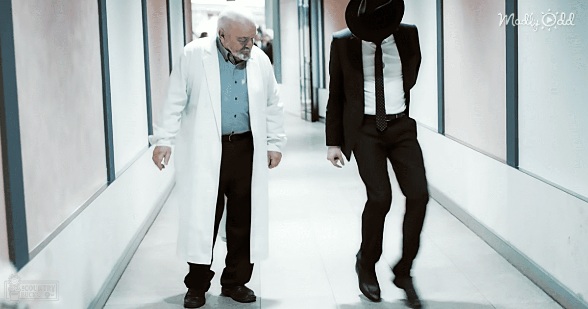 An older adult male in a white lab coat walks alongside another person dressed as Michael Jackson down a modern indoor hallway.