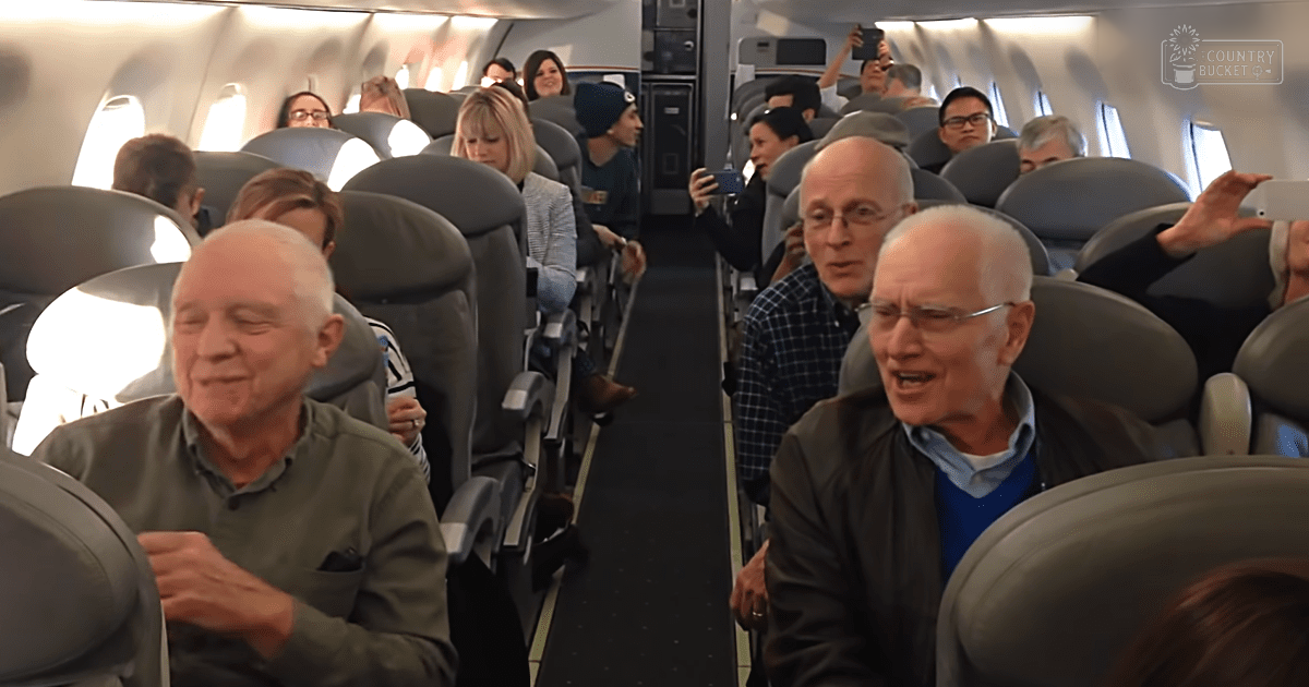 Two older adults seated in an airplane cabin, interacting during a daytime flight with natural light coming through windows.