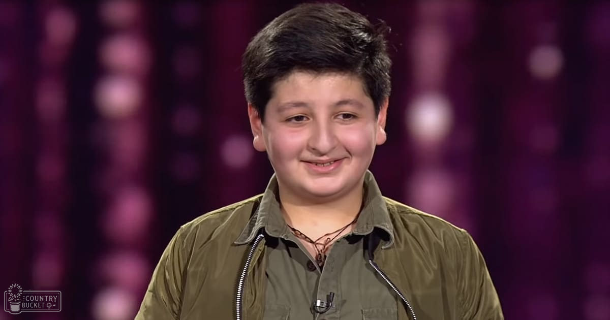 A child (8-12) wearing an olive-green jacket with a buttoned shirt underneath, standing indoors against a purple backdrop.