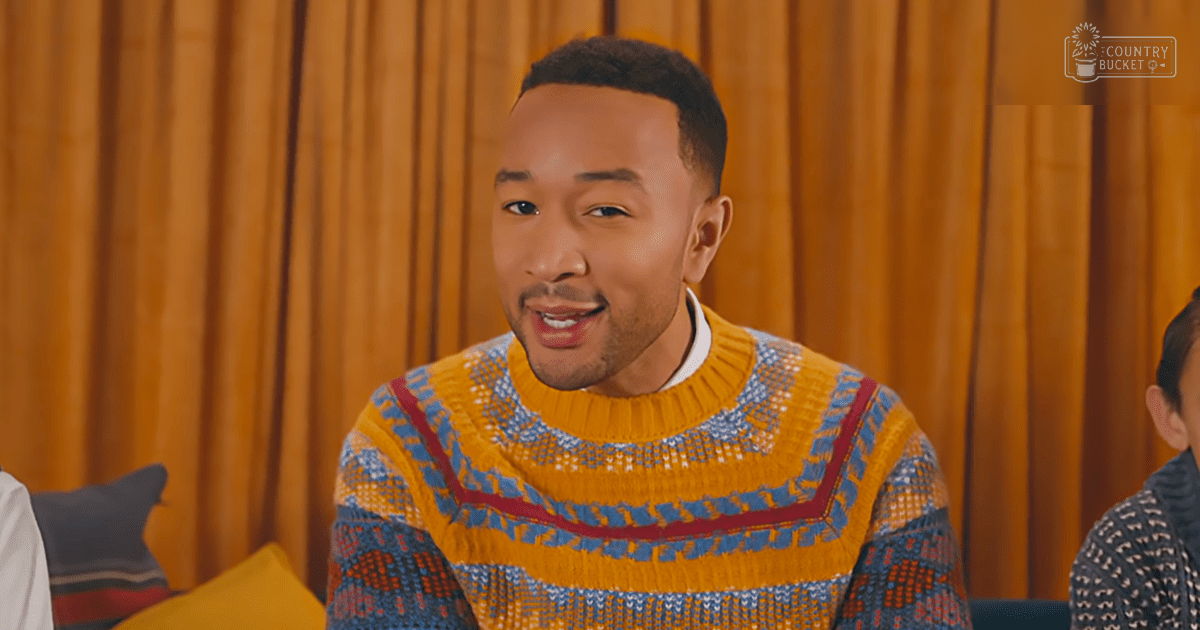 A young adult male wearing a colorful geometric-patterned sweater indoors with other partially visible individuals and home furnishings.