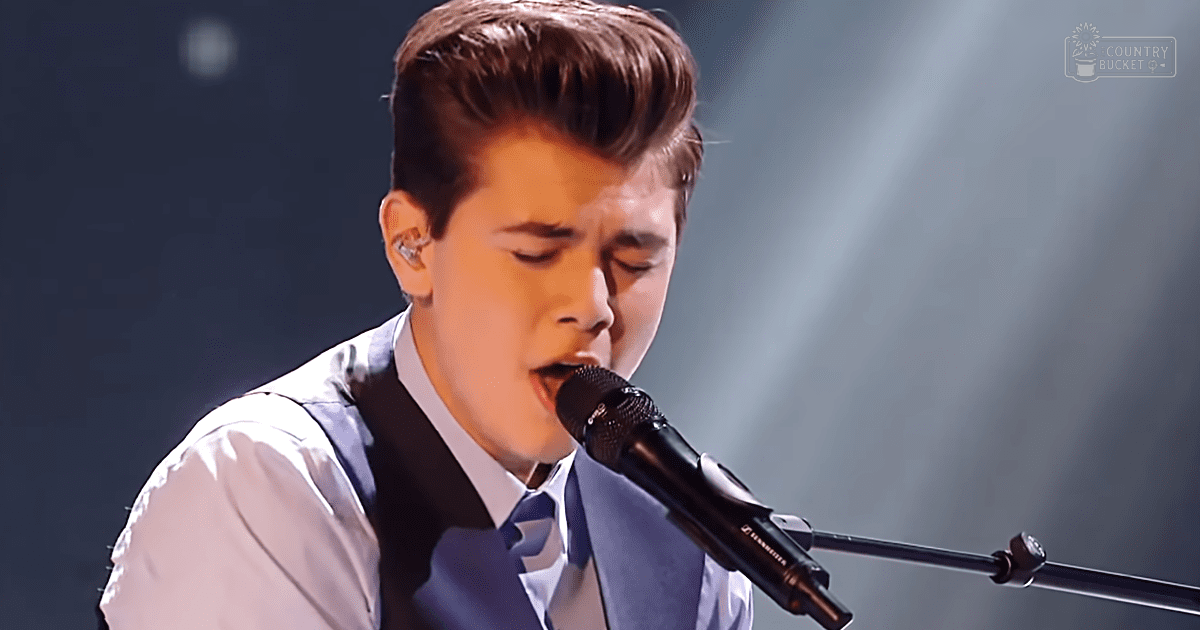A young adult male in formal attire performs on a stage under dramatic lighting, with 'Madly Odd' text visible in the background.