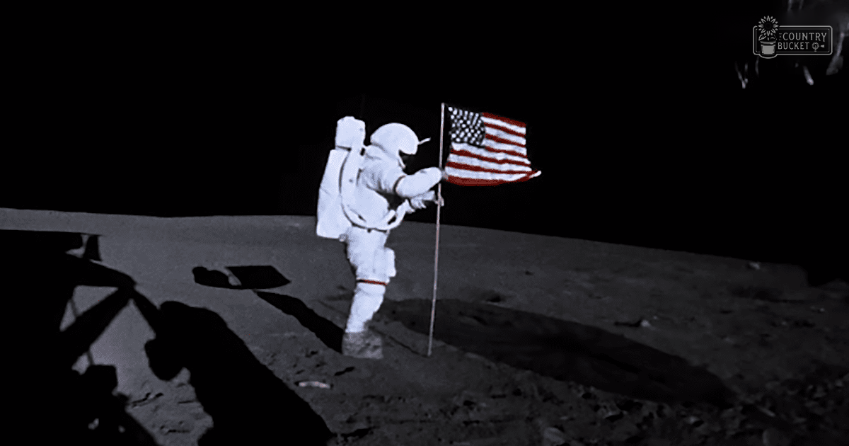 Astronaut planting an American flag on the moon's surface at night with a dark sky in the background.