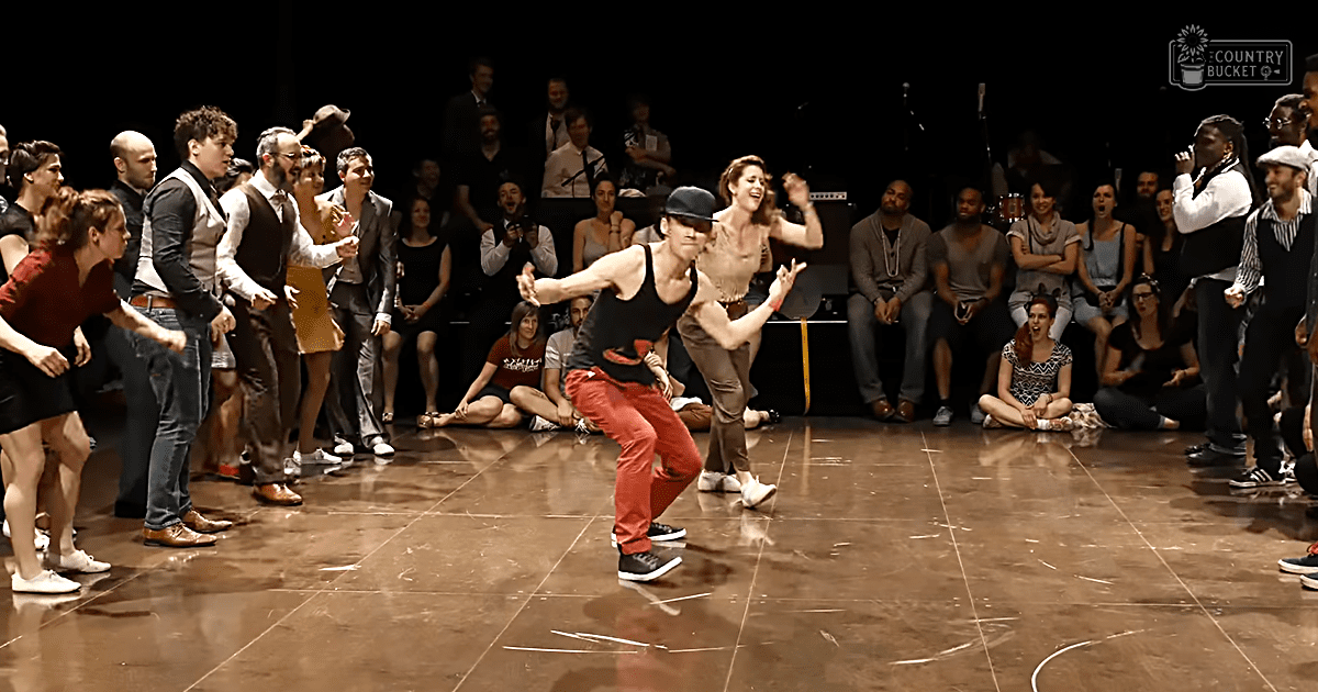 Indoor dance performance with young to middle-aged audience in a polished wooden floor space, possibly evening event.