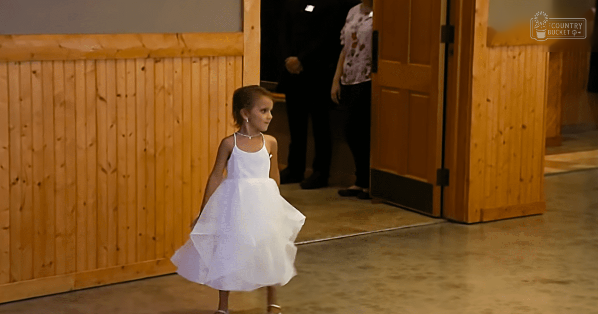 A young girl wearing a white sleeveless dress at an indoor event with wooden paneling and rustic decor.