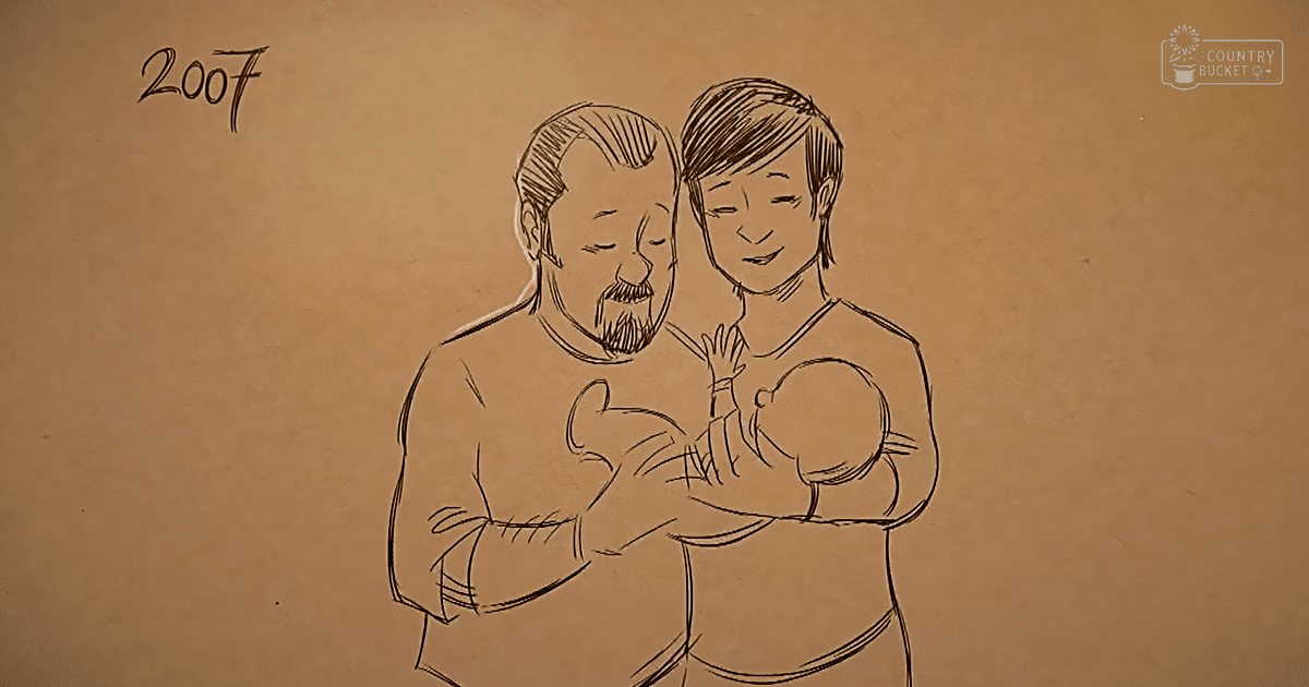 A family scene from 2007 with an adult male in a long-sleeved shirt and a middle-aged adult female holding an infant against a plain brown background.