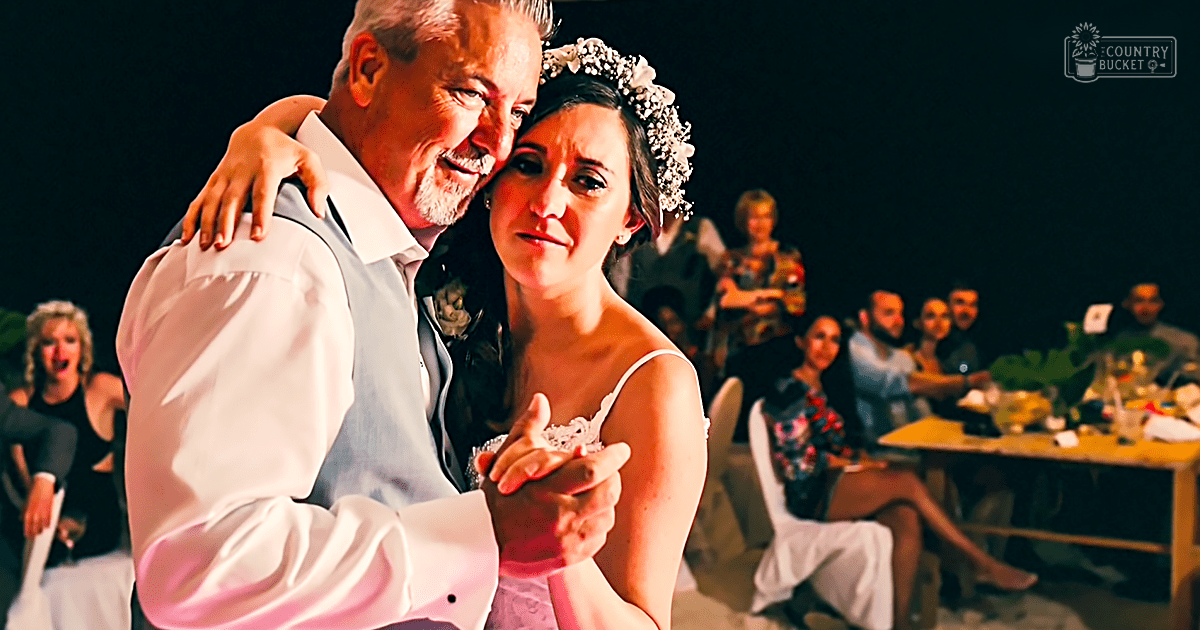 A bride and her father dancing at an outdoor wedding reception during evening. The bride wears a white strapless wedding dress with a floral crown, while the father is in a light-colored suit jacket.