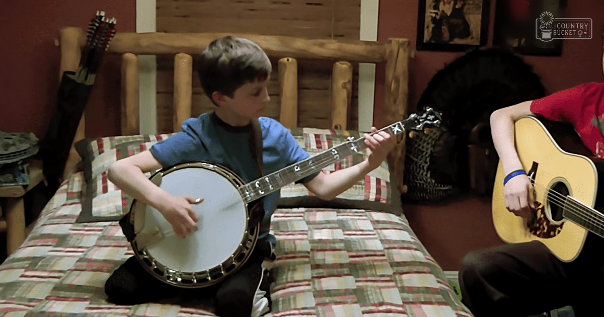 A child playing a banjo in a bedroom with wooden walls and decor suggesting a cozy atmosphere.