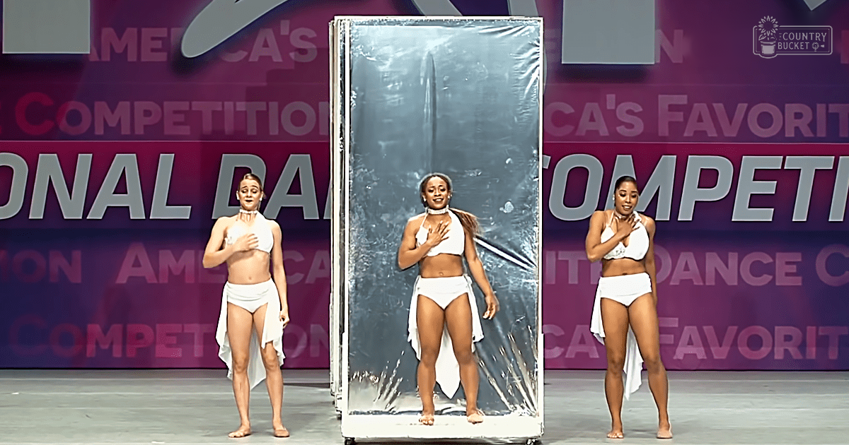 Three young adult females performing a dance routine at America's Favorite Dance Competition on an indoor stage with banners in the background.