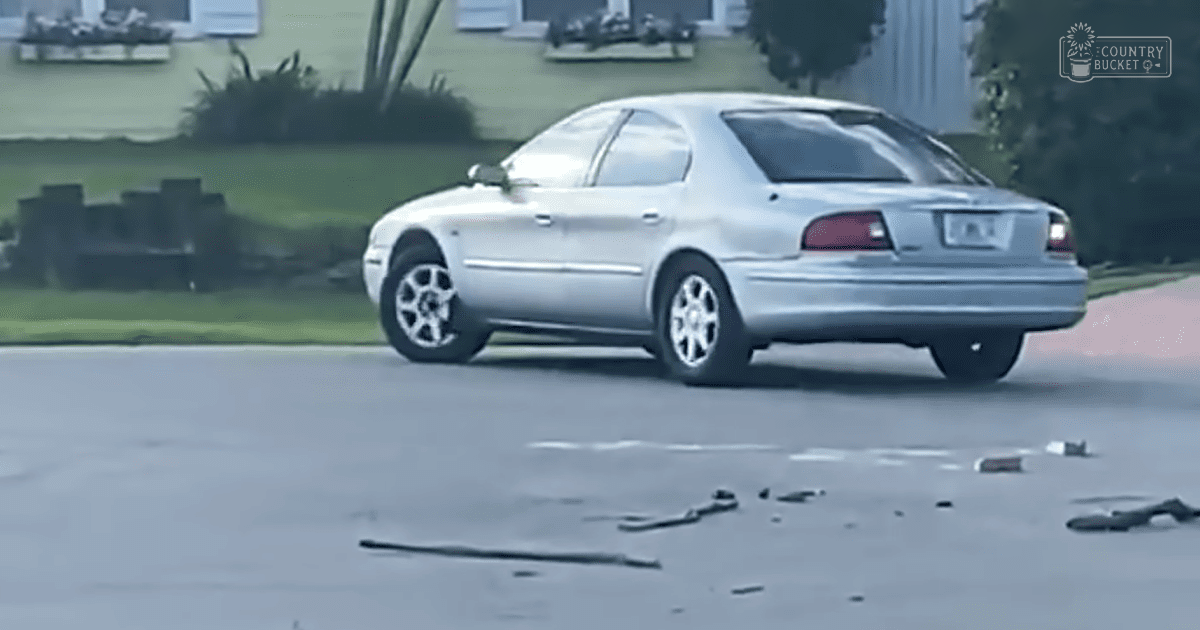 A silver sedan parked in a residential driveway with scattered debris, soft daylight illuminating a late afternoon scene