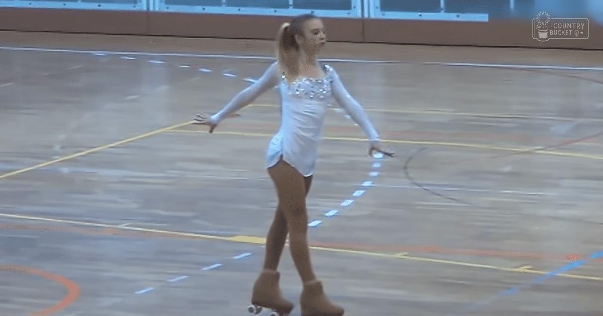 A young adult female roller skater in a white figure skating leotard with embellishments, performing on an indoor polished wooden gymnasium floor marked for sports activities.