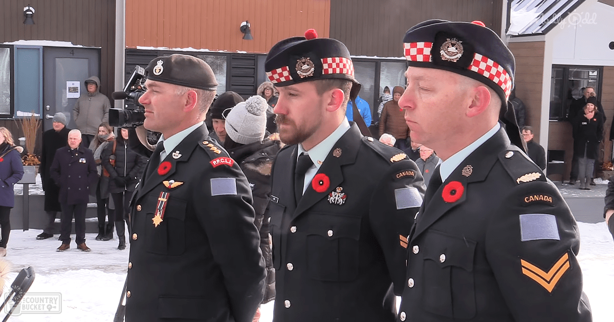 An outdoor winter scene at a military ceremony with several adults in dark green military uniforms, each wearing a black or checkered red-and-white beret adorned with poppy pins and badges.