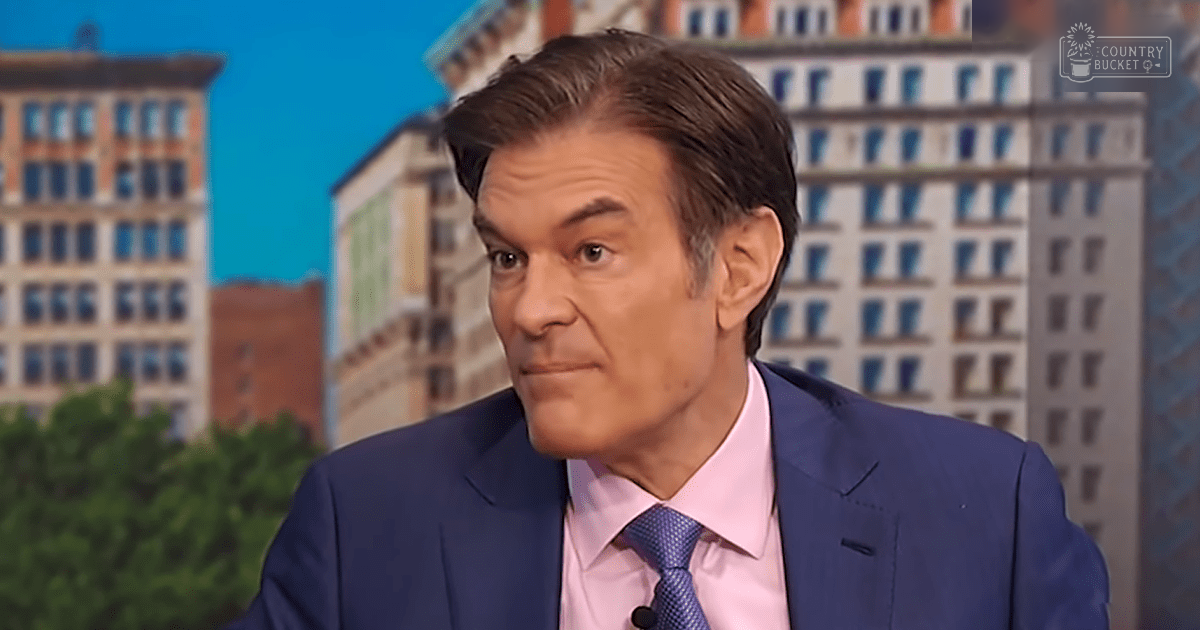 A middle-aged adult male wearing a tailored blue suit jacket with a subtle dot-patterned pink shirt stands against a cityscape backdrop in an indoor studio setting during what appears to be daytime.