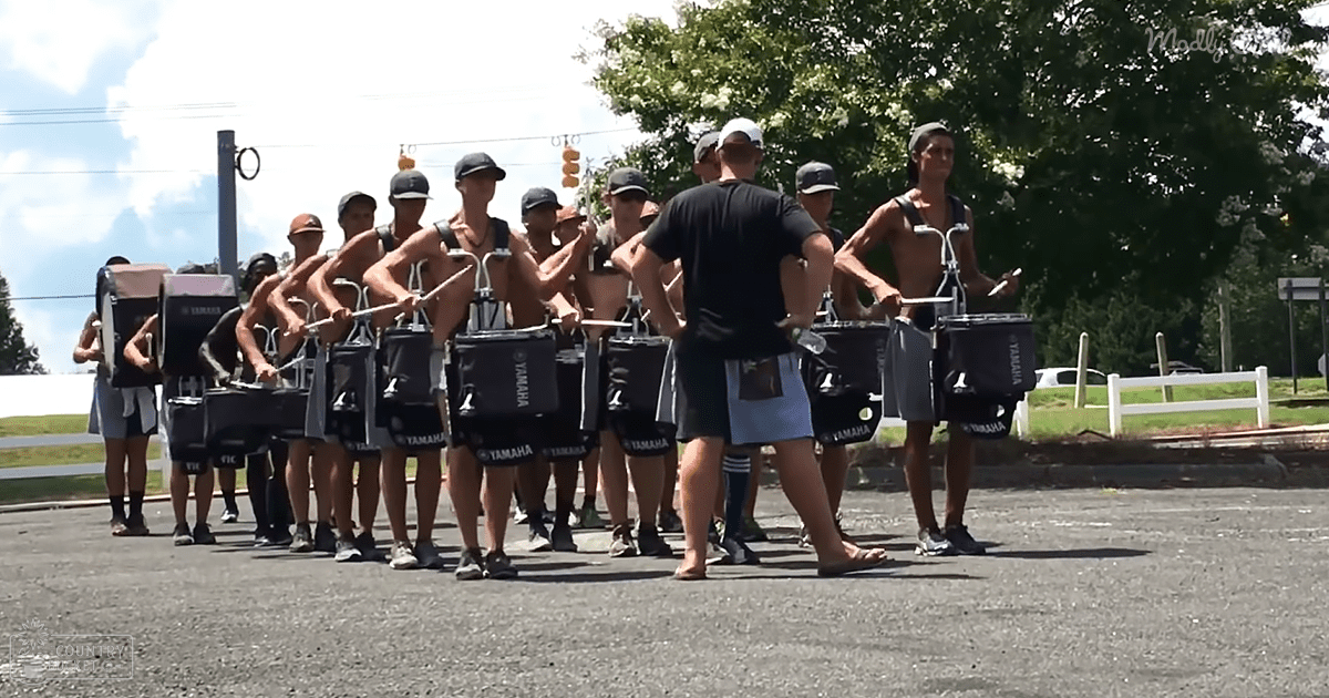 Teenage male drummers practicing outdoors in a parking lot under bright summer sunlight.