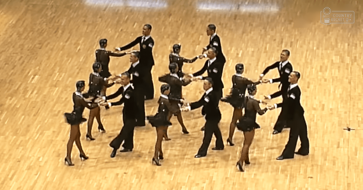 Young adult dancers performing in an indoor arena with wooden floors and focused lighting.