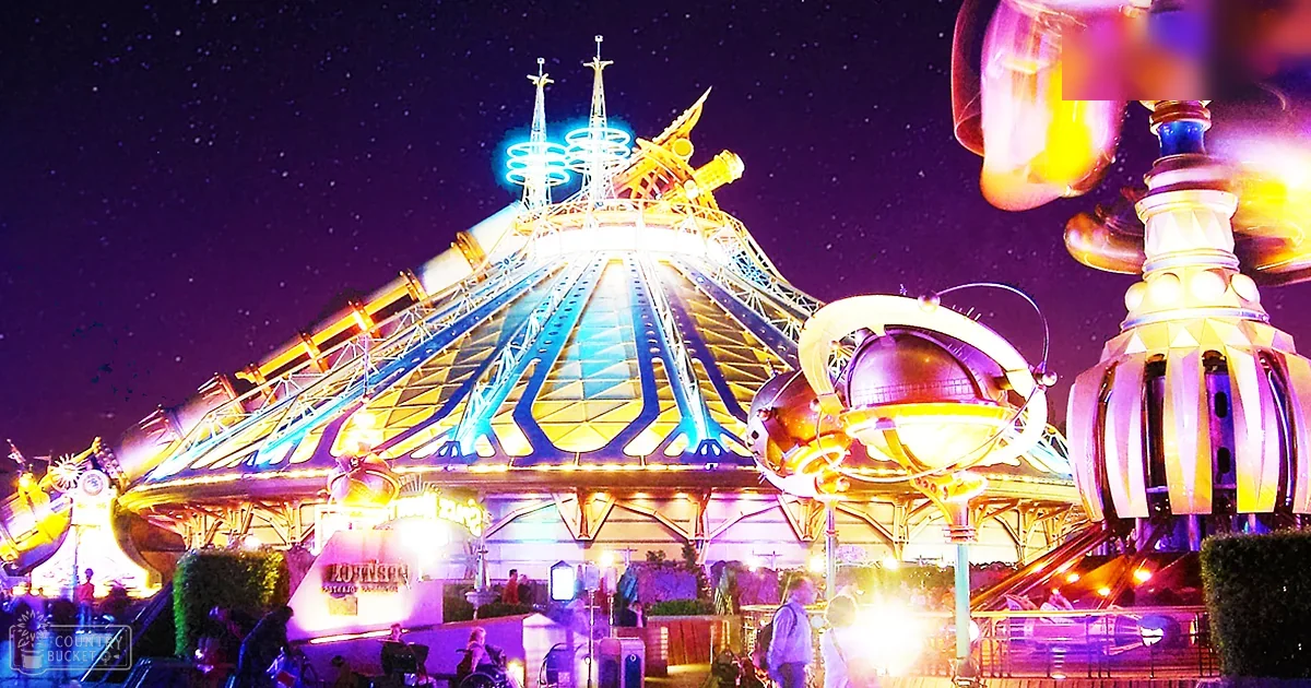 A nighttime view of Space Mountain at Disneyland with several visitors exploring the entrance area under neon lights and signage.