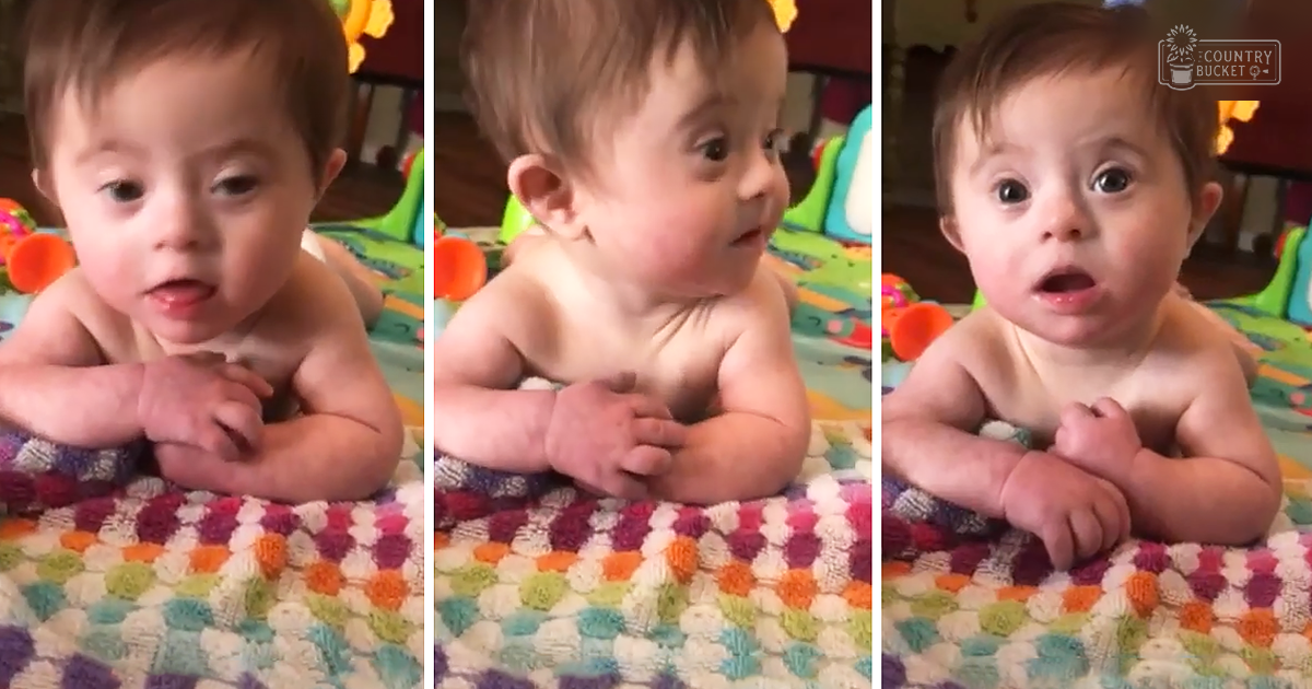 An infant male, shirtless, lying on a colorful blanket indoors with natural lighting and toys in the background.