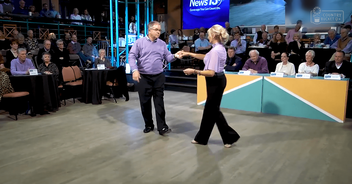 Adult male singer dancing with an adult female dancer on a stage with 'News 13' displayed behind them, suggesting a television show or dance competition setting.