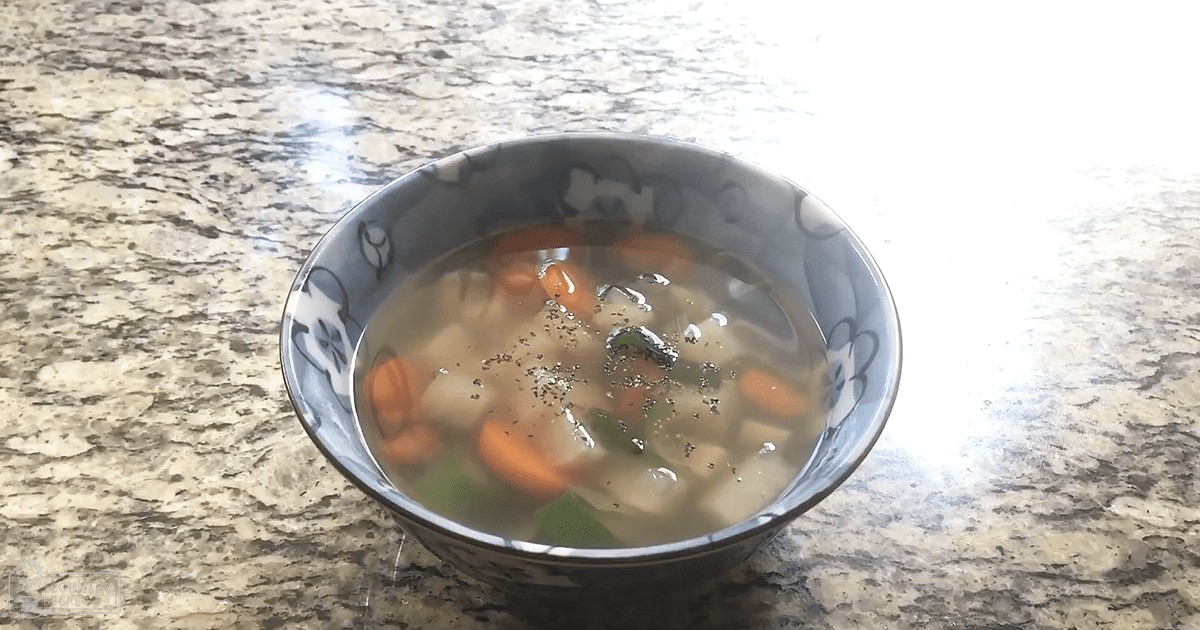A bowl of vegetable soup on a granite countertop in a kitchen setting.