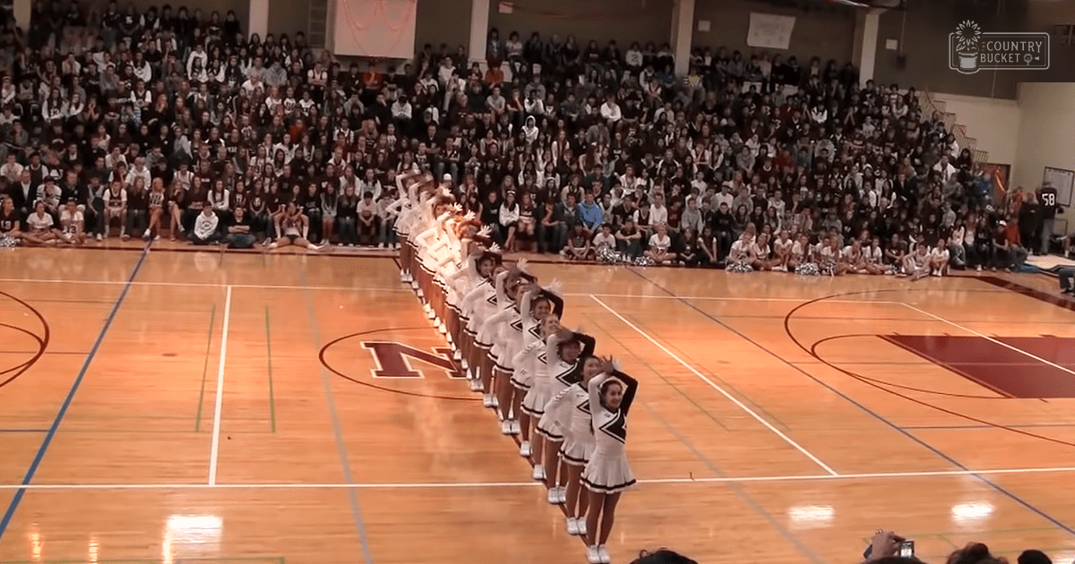 Cheerleaders performing in a gymnasium with an audience watching, indoors during daytime or early evening under indoor lighting.