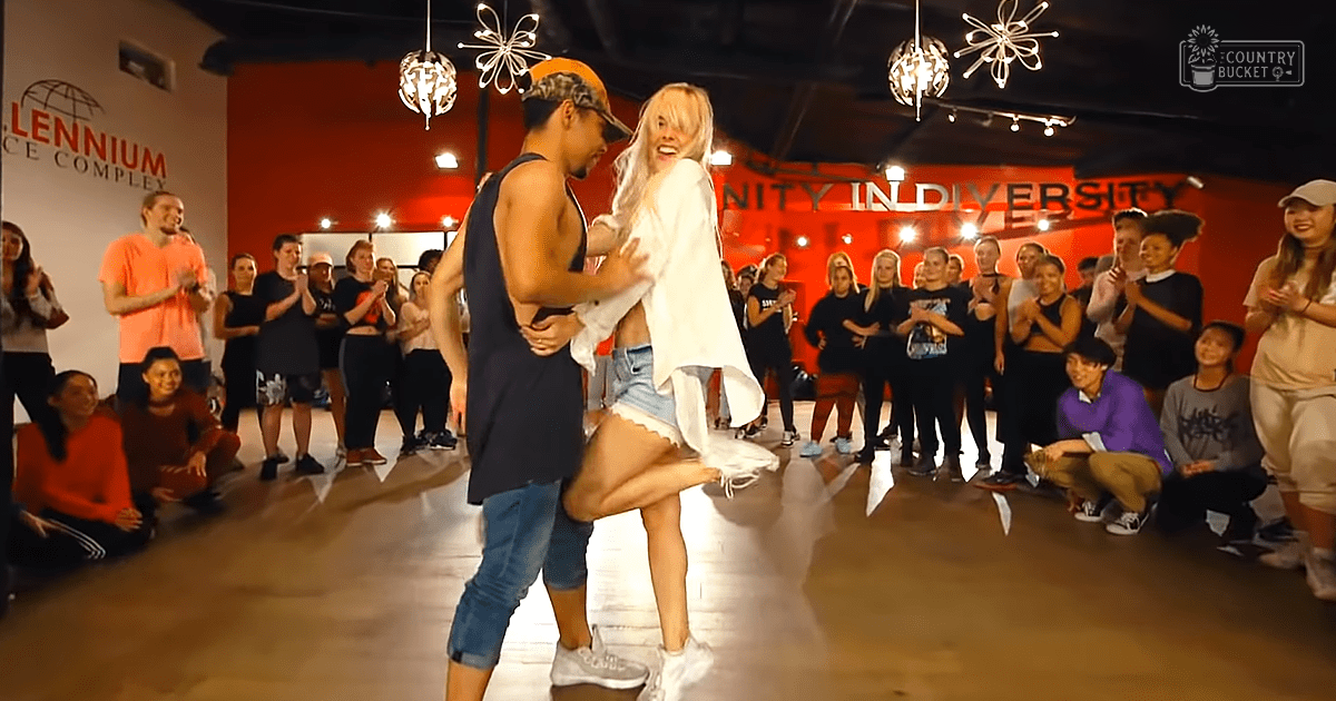 A dance class or performance at Millennium Dance Complex with dancers wearing casual attire and an audience watching indoors under artificial lighting.