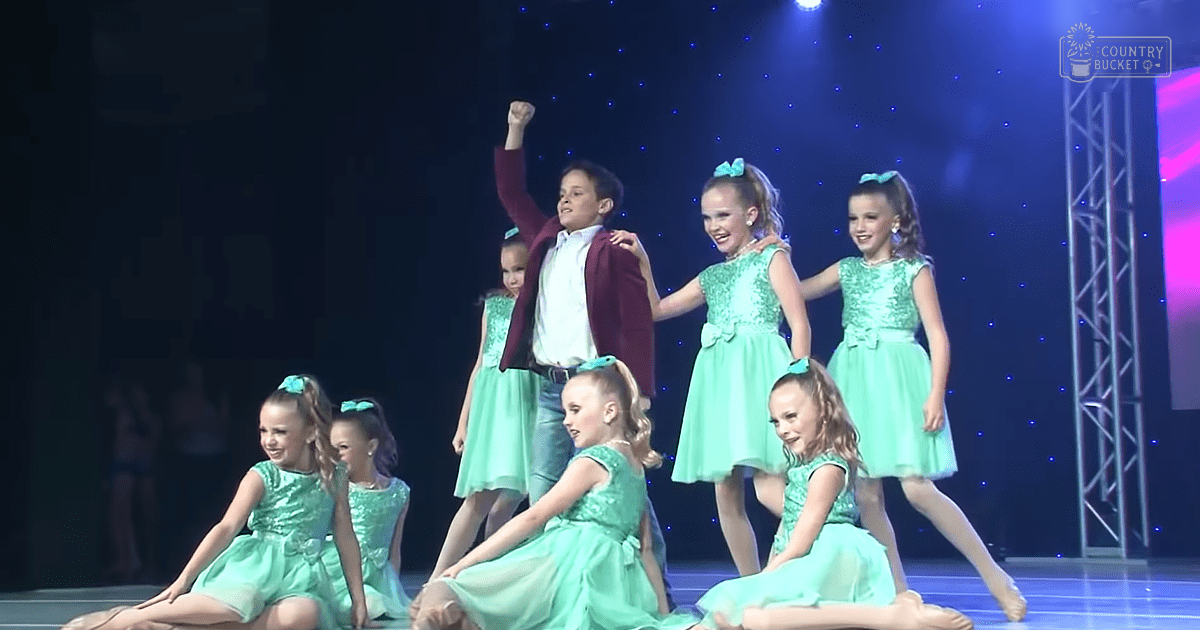 Group of children in light green dresses performing on an indoor stage with a blue starry backdrop with the text 'Molly Odd'