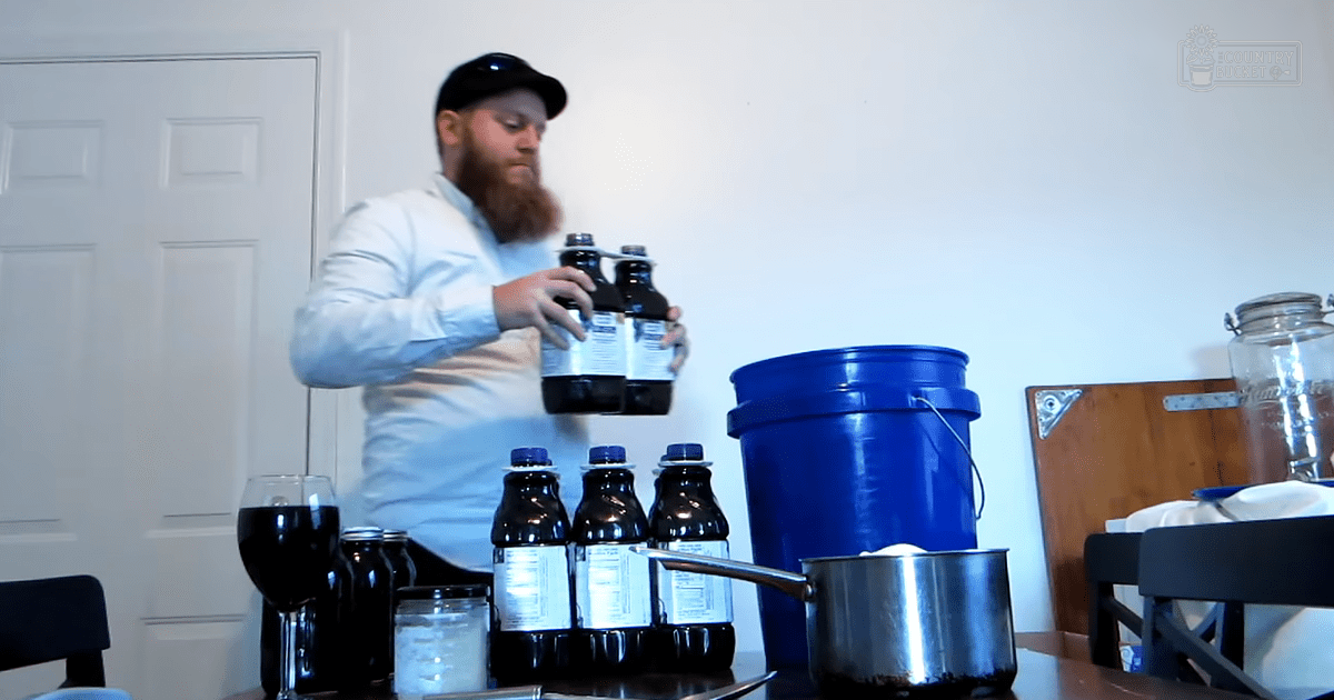 An adult male in a modern white button-up shirt indoors, surrounded by kitchen items like bottles and a blue bucket.