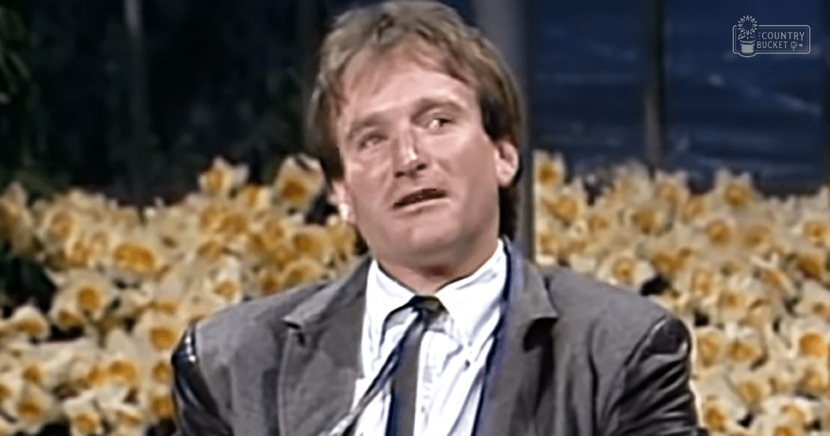 Middle-aged adult male wearing a classic fit dark gray suit jacket with a high collar and lapels, standing indoors against a backdrop of decorative flowers.