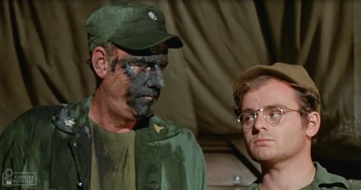 Middle-aged male in a green military jacket with patch, young adult to middle-aged male wearing glasses and similar uniform style, set against a tent-like structure suggesting an outdoor wartime camp, natural daylight illuminating the scene.