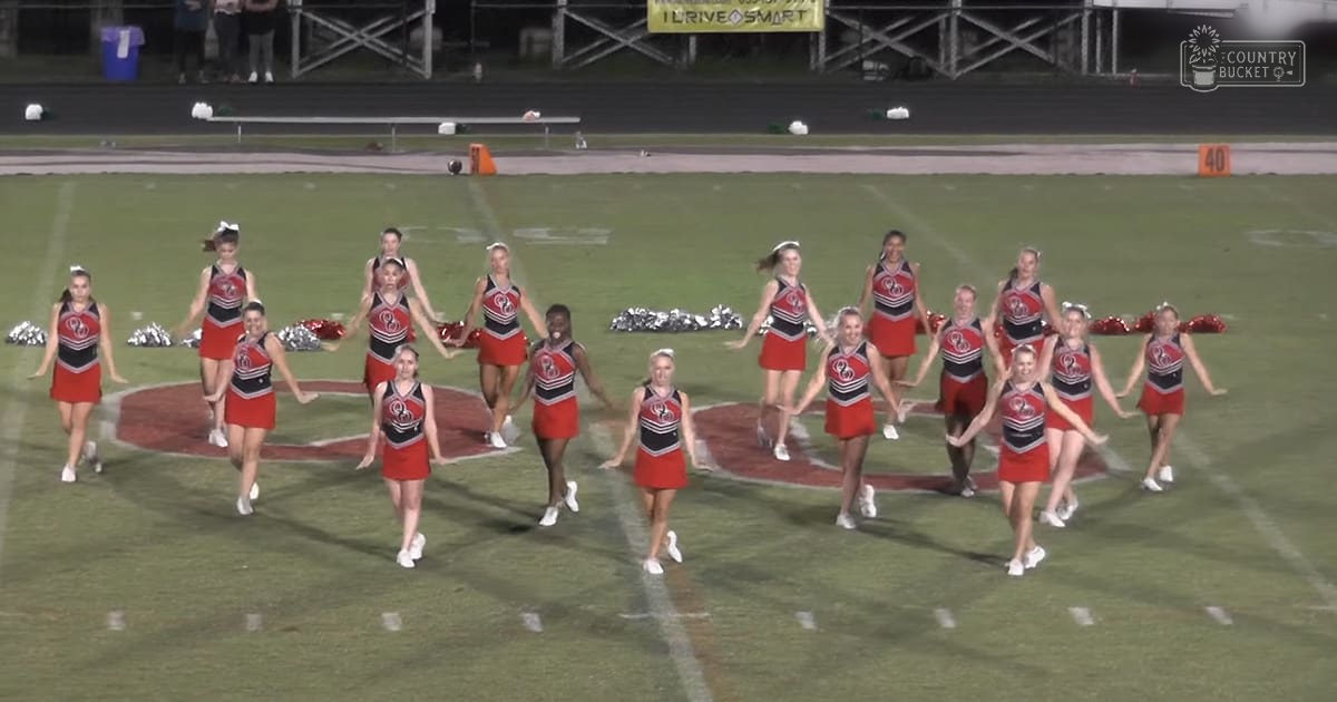 A nighttime football field scene with a cheerleading team performing, under artificial lighting.
