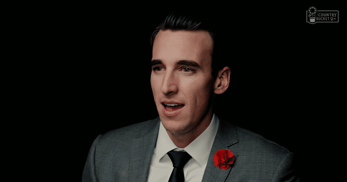 A young adult male in a tailored gray suit with a red lapel pin, set against a dark background, emphasizing formal attire suitable for business or special occasions.
