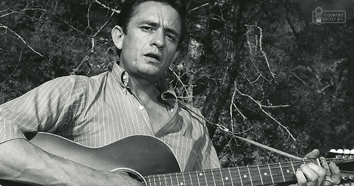 A middle-aged man playing a guitar outdoors with bare trees suggesting late autumn or winter, text reading 'Madly Odd' in the top right corner.