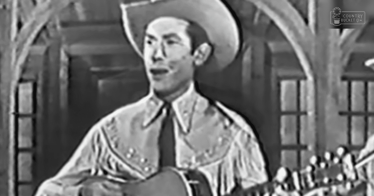 A young adult male wearing a cowboy hat and intricately embroidered shirt indoors with rustic Western decor.