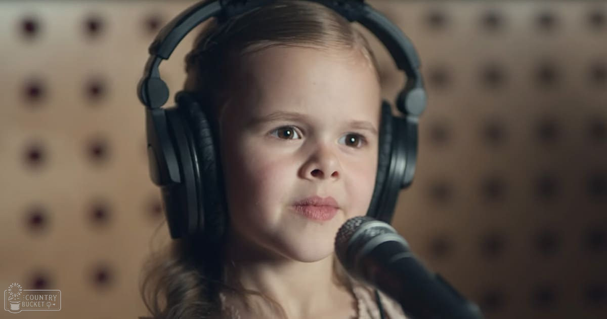 A young child with light-colored hair in a recording studio setting, wearing large black over-ear headphones.