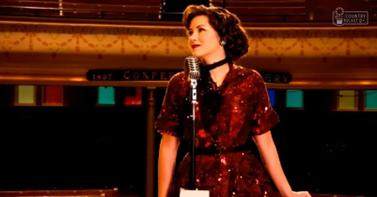 A woman in a dark red dress with floral patterns and black accessories sings on stage, surrounded by ornate wall decorations and stained glass windows.