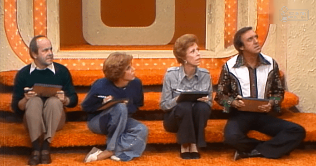 Adults seated on an orange sofa in a television studio set during daytime, wearing various casual clothing and holding clipboards.