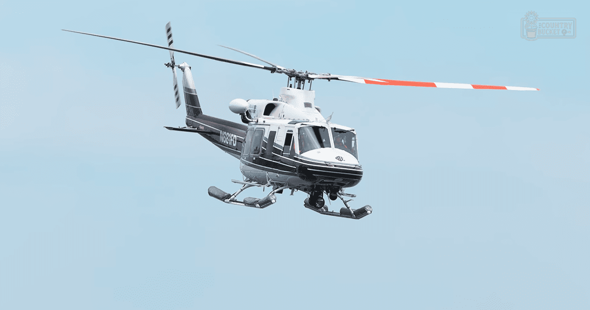 A helicopter soars against a backdrop of a clear blue sky with white and black rotor blades and a red stripe, suggesting an outdoor setting in spring or summer under natural daylight.